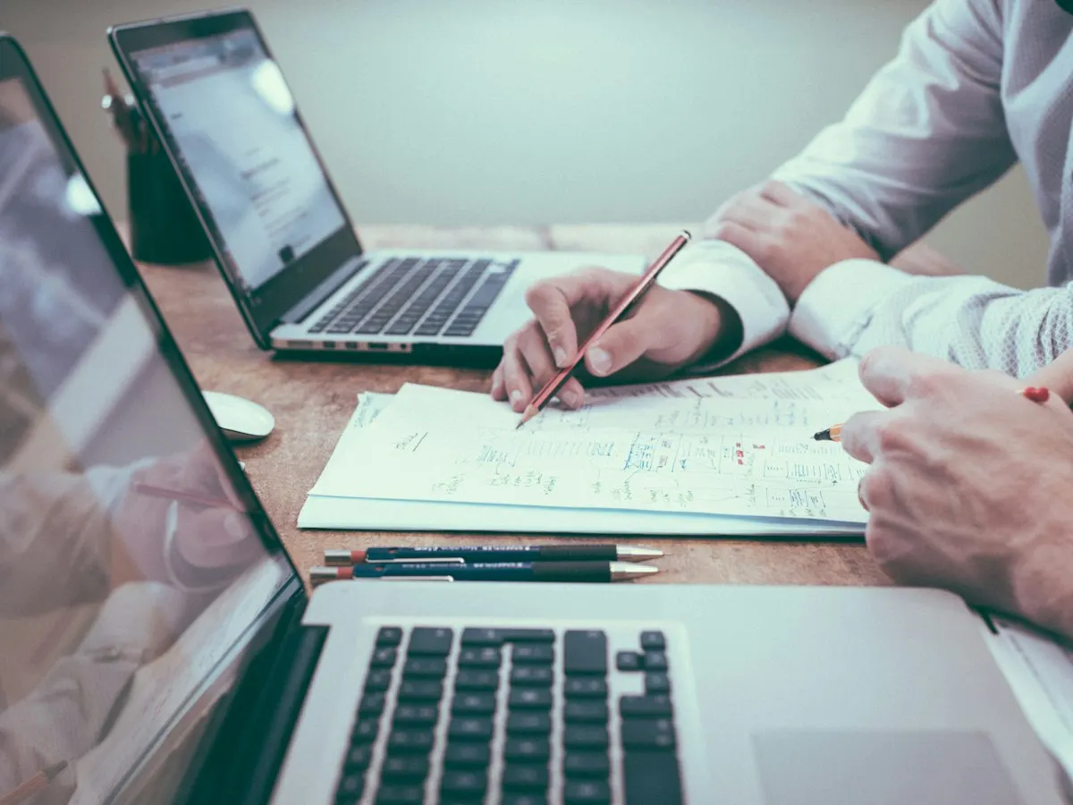 Twee mensen werken aan een bureau met laptops en papieren aantekeningen