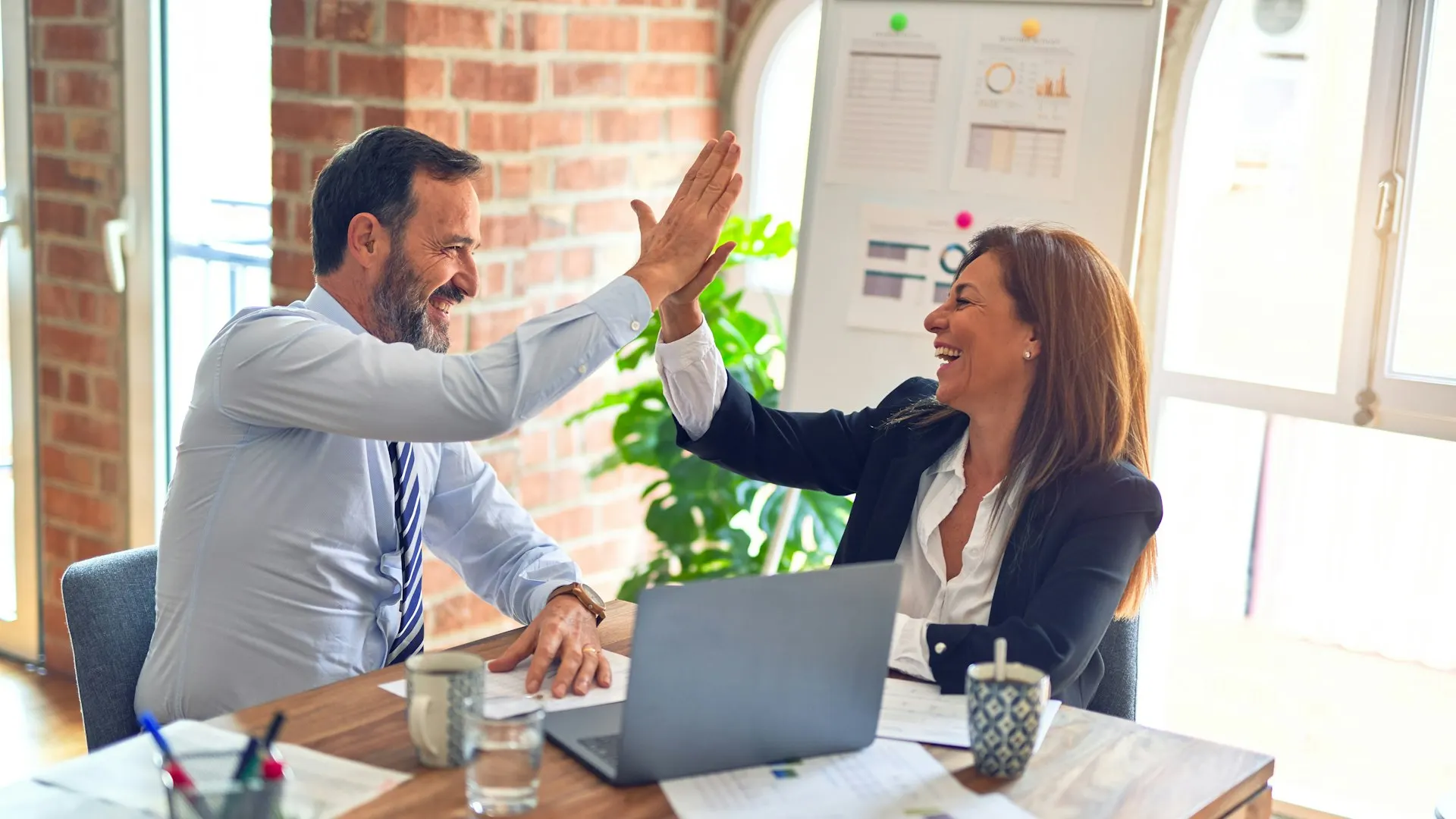 Een man en een vrouw geven elkaar een high five aan een tafel na een geslaagd gesprek