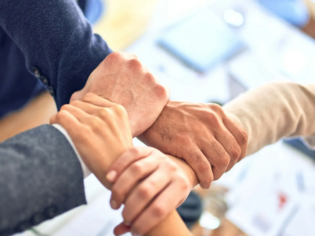 Handen van collega's die elkaar vasthouden boven een tafel