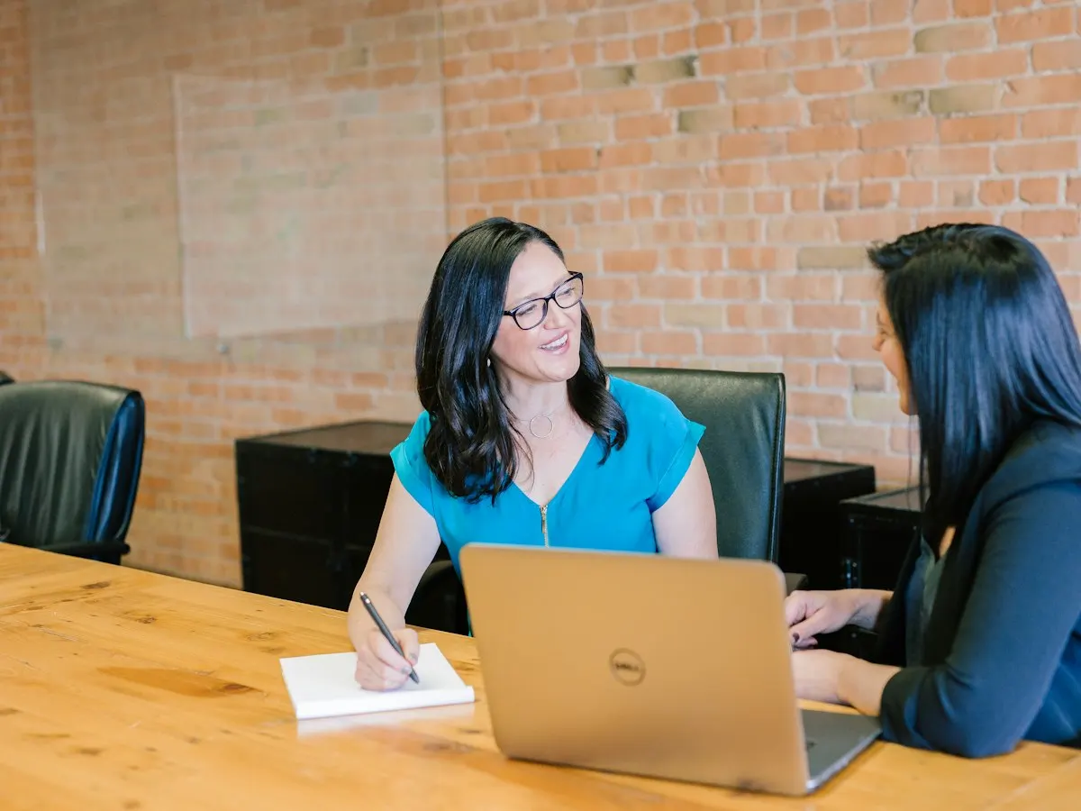 Twee vrouwen in gesprek aan een tafel met een laptop